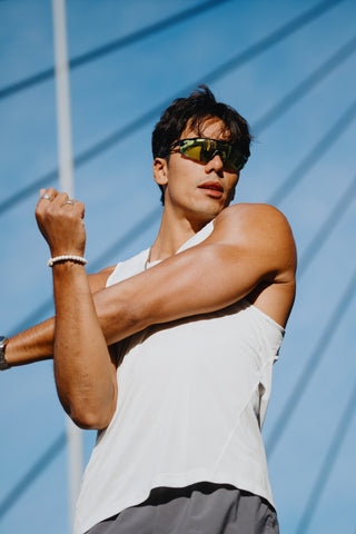Person wearing sunglasses and a white tank top against a blue sky.