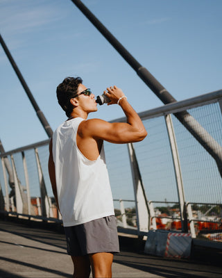 Man drinking a supplement from a water bottle on a bridge with a clear blue sky