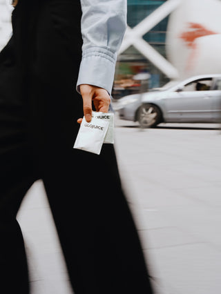 Person holding a white packet with 'GLOJUICE' branding in an urban setting.