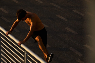 Man stretching on a metal railing against a dark background